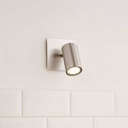 Wall-mounted light fixture on a tiled kitchen wall with bottles and a wooden spoon.