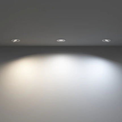 Three recessed lights on a ceiling casting light on a wall.