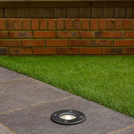 Outdoor lighting fixture on a paved patio with grass and brick wall in the background