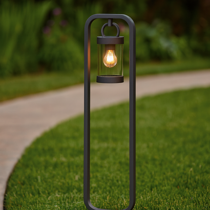Black outdoor lamp post with a lit bulb on grass and pathway